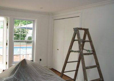 a room being painted, ladders up, and tarp covering furniture