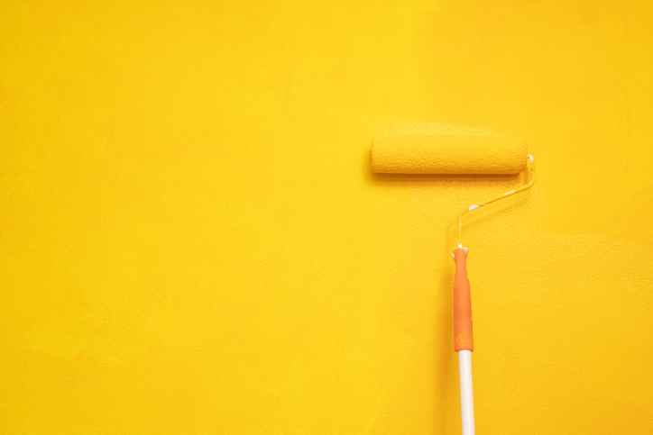 A paint roller applying yellow paint on a wall